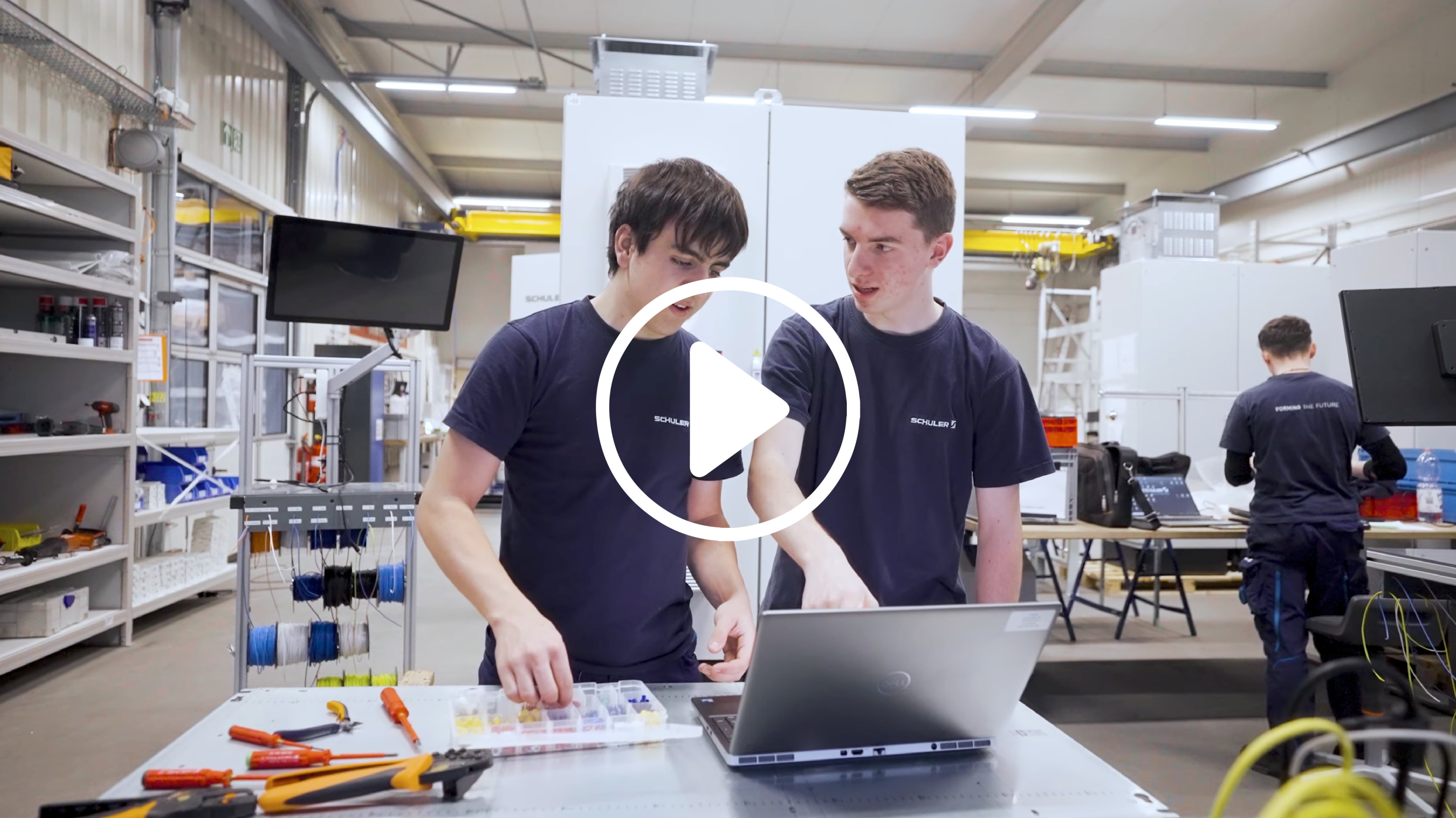 zwei Lernende Automatiker, stehen während einer Besprechung in der Produktion. Rundum sind Maschinen und Werkzeuge zusehen.